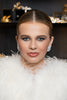 Woman with styled hair and makeup, wearing a white feathered garment, with decorative background.